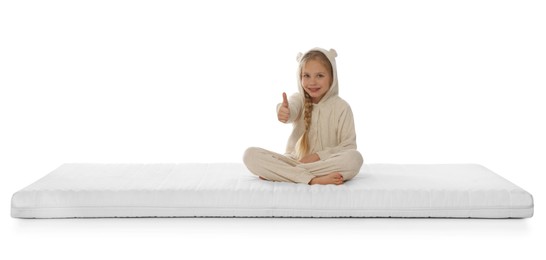 Little girl sitting on mattress and showing thumb up against white background