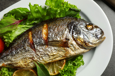 Delicious roasted fish with lemon and lettuce on plate, closeup view