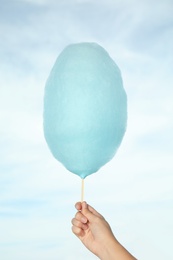 Photo of Woman holding sweet cotton candy on blue sky background, closeup view