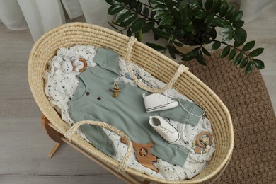 Cute baby clothes and accessories in basket bassinet at home, top view