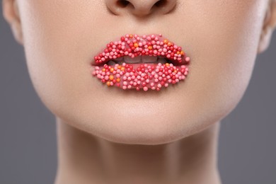 Young woman with beautiful lips covered confectionery sprinkles on gray background, closeup