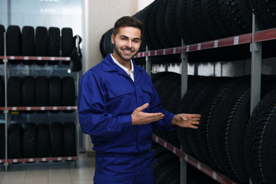 Male mechanic near rack with tires in auto store