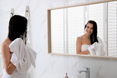 Happy young woman drying hair with towel after washing near mirror in bathroom