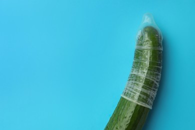 Cucumber with condom on light blue background, top view and space for text. Safe sex concept