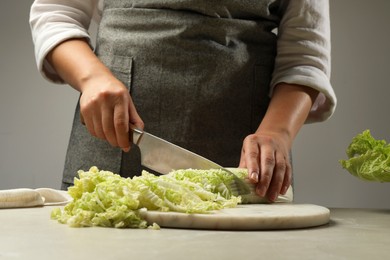 Photo of Woman cutting fresh Chinese cabbage at light grey table, closeup