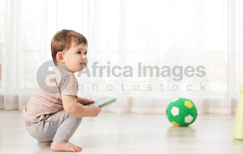 Photo of Cute baby sitting on floor with book at home