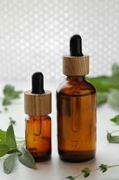 Bottles of essential oils and fresh herbs on white table