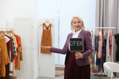 Female business owner holding OPEN sign in boutique