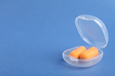 Pair of orange ear plugs in case on blue background. Space for text