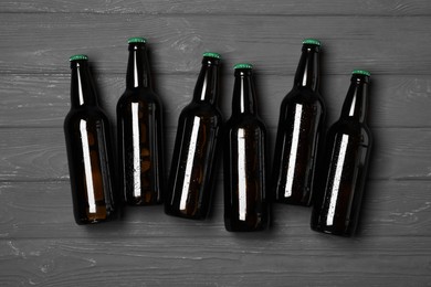 Photo of Glass bottles of beer on grey wooden background, flat lay
