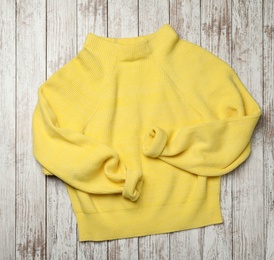 Photo of Beautiful yellow warm sweater on white wooden table, top view