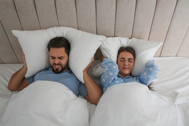 Young couple suffering from noisy neighbours in bed at home, above view