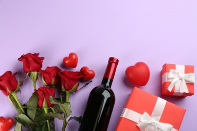 Flat lay composition with beautiful red roses and bottle of wine on violet background, space for text. Valentine's Day celebration