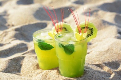 Glasses of refreshing drink with kiwi and mint on sand