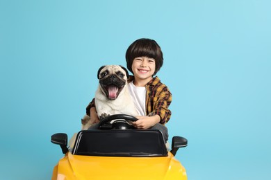 Little boy with his dog in toy car on light blue background