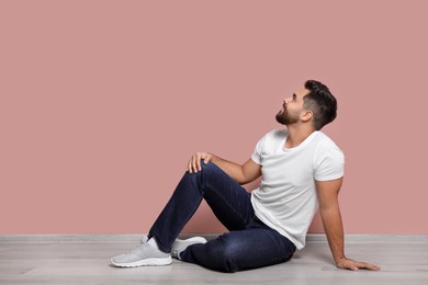 Young man sitting on floor near pink wall indoors. Space for text