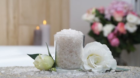 Glass with bath salt and beautiful flowers on wicker mat in bathroom