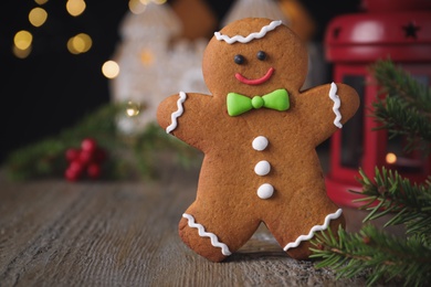 Gingerbread man on wooden table against blurred lights, closeup. Space for text