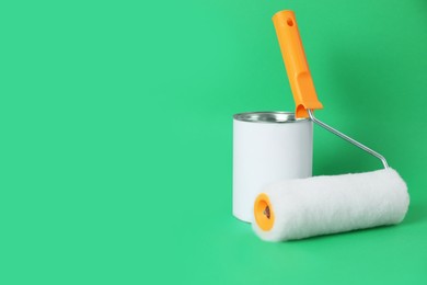 Photo of Can of orange paint and roller brush on green background. Space for text