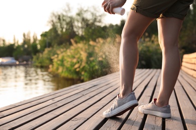 Woman applying insect repellent onto leg at pier, closeup. Space for text