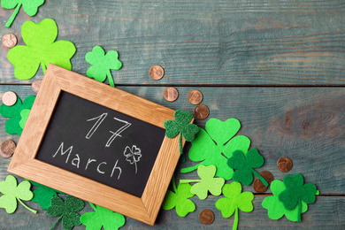 Chalkboard with written 17 March, clover leaves and gold coins on blue wooden background. St. Patrick's Day celebration