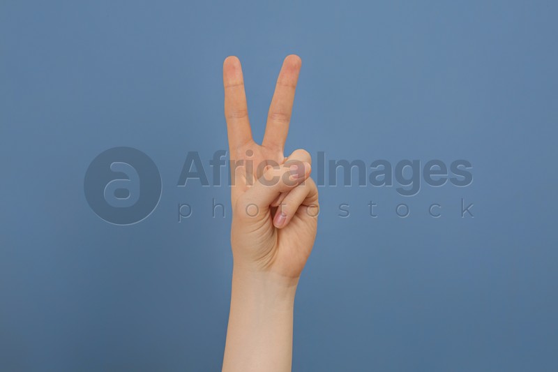 Photo of Woman showing two fingers on pale blue background, closeup
