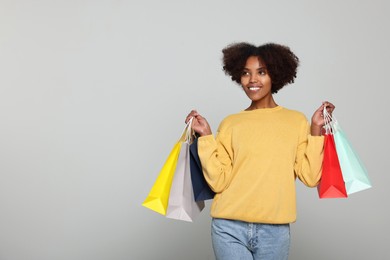 Photo of Happy African American woman with shopping bags on light grey background. Space for text