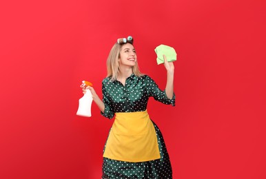 Young housewife with detergent and rag on red background
