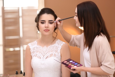 Professional makeup artist working with young bride in salon