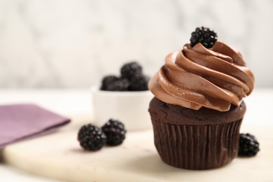 Delicious chocolate cupcake with cream and blackberries on white board, closeup. Space for text