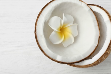 Halves of coconut and flower on white wooden background