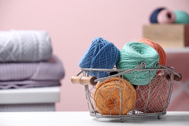Colorful clews of threads in basket on table against blurred background, space for text