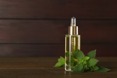 Glass bottle of nettle oil with dropper and leaves on wooden table. Space for text