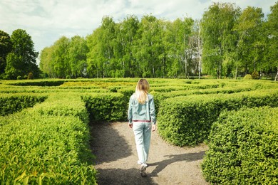 Photo of Young woman in hedge maze on sunny day, back view