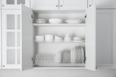 Photo of Open cabinet with different clean plates and bowls in kitchen