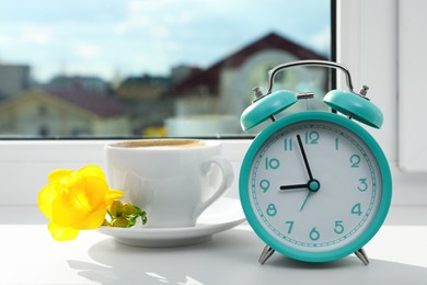 Alarm clock and cup of drink with flower on windowsill. Good morning