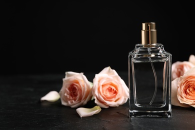 Bottle of perfume and beautiful roses on black table. Space for text