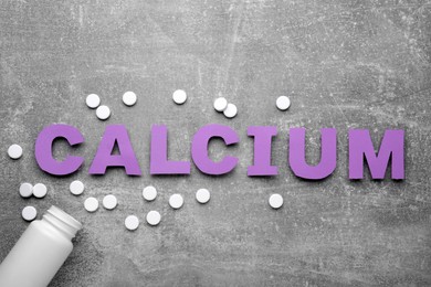 Word Calcium made of violet paper letters, medical bottle and pills on gray background, top view