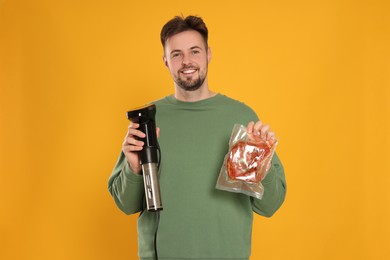 Photo of Smiling man holding sous vide cooker and meat in vacuum pack on orange background