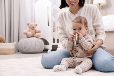 Young mother and her baby with teether on floor at home. Space for text