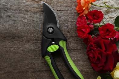 Photo of Secateur and beautiful roses on wooden table, flat lay
