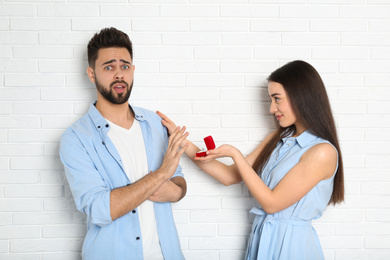 Young man rejecting engagement ring from girlfriend near white brick wall