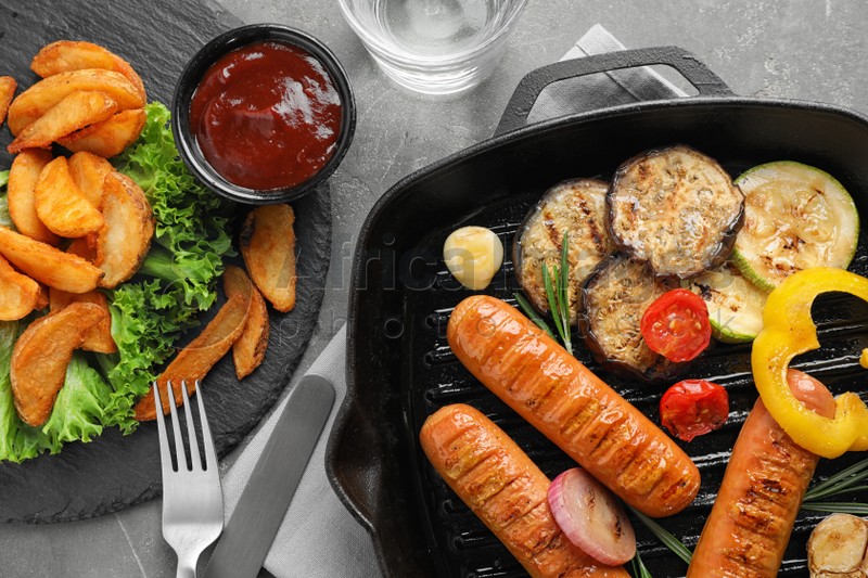 Delicious grilled sausages and vegetables on grey table, flat lay