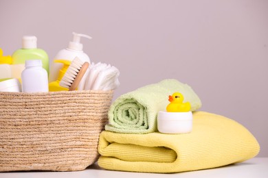 Wicker basket with baby cosmetic products, bath accessories and rubber duck on white table against grey background