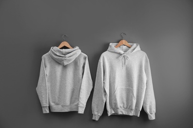 New hoodie sweaters with hangers on grey wall. Mockup for design
