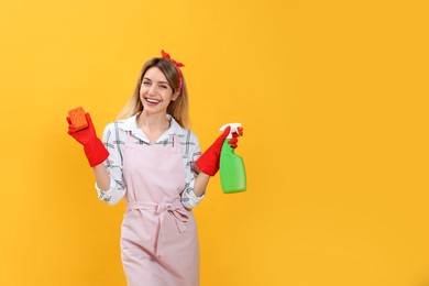 Photo of Young housewife with detergent and sponge on yellow background. Space for text