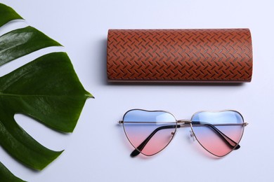 Stylish elegant heart shaped sunglasses and brown leather case with pattern on white background, flat lay