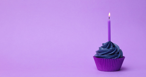 Delicious birthday cupcake with dark blue cream and burning candle on violet background. Space for text