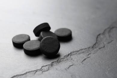 Activated charcoal pills on black table, space for text. Potent sorbent