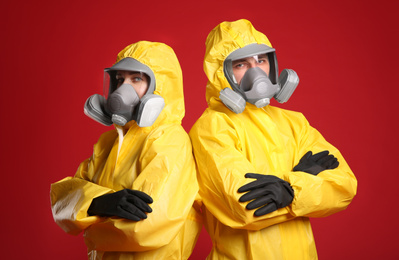 Man and woman wearing chemical protective suits on red background. Virus research